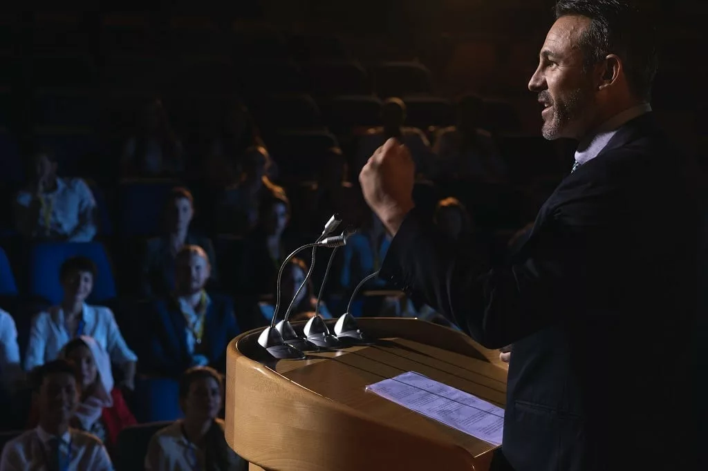 A man standing and giving presentation in the auditorium.