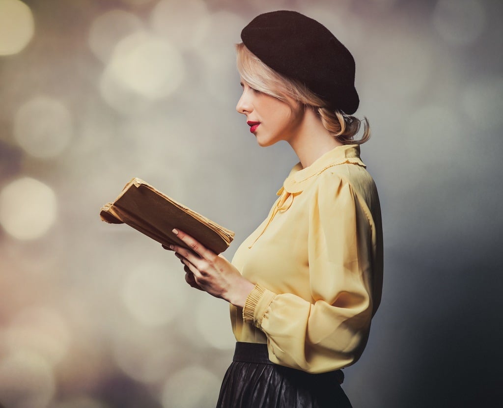 Beautiful girl in vintage clothes with book on gray background.
