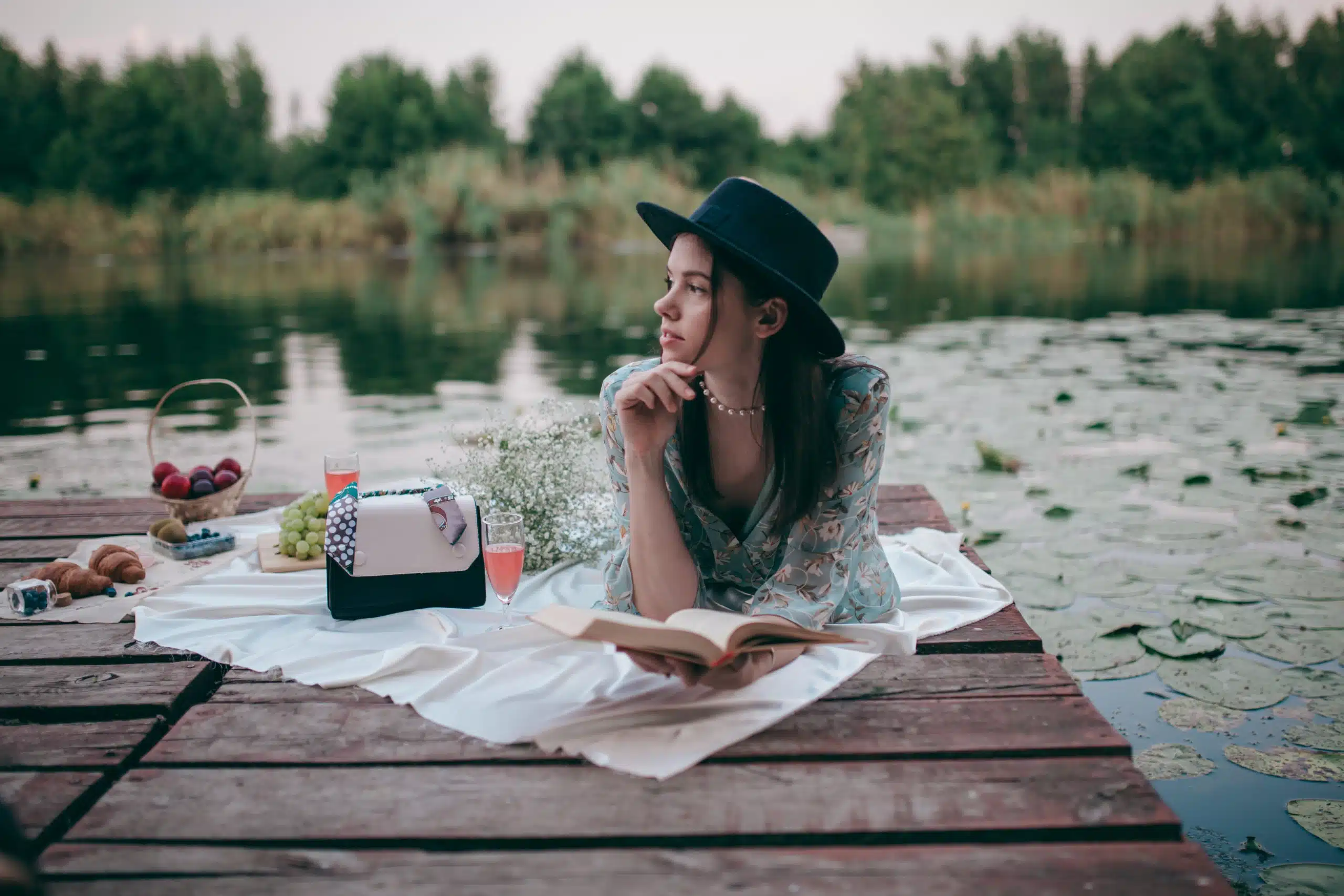 Girl on a picnic by the lake drinks rose wine and reads a book