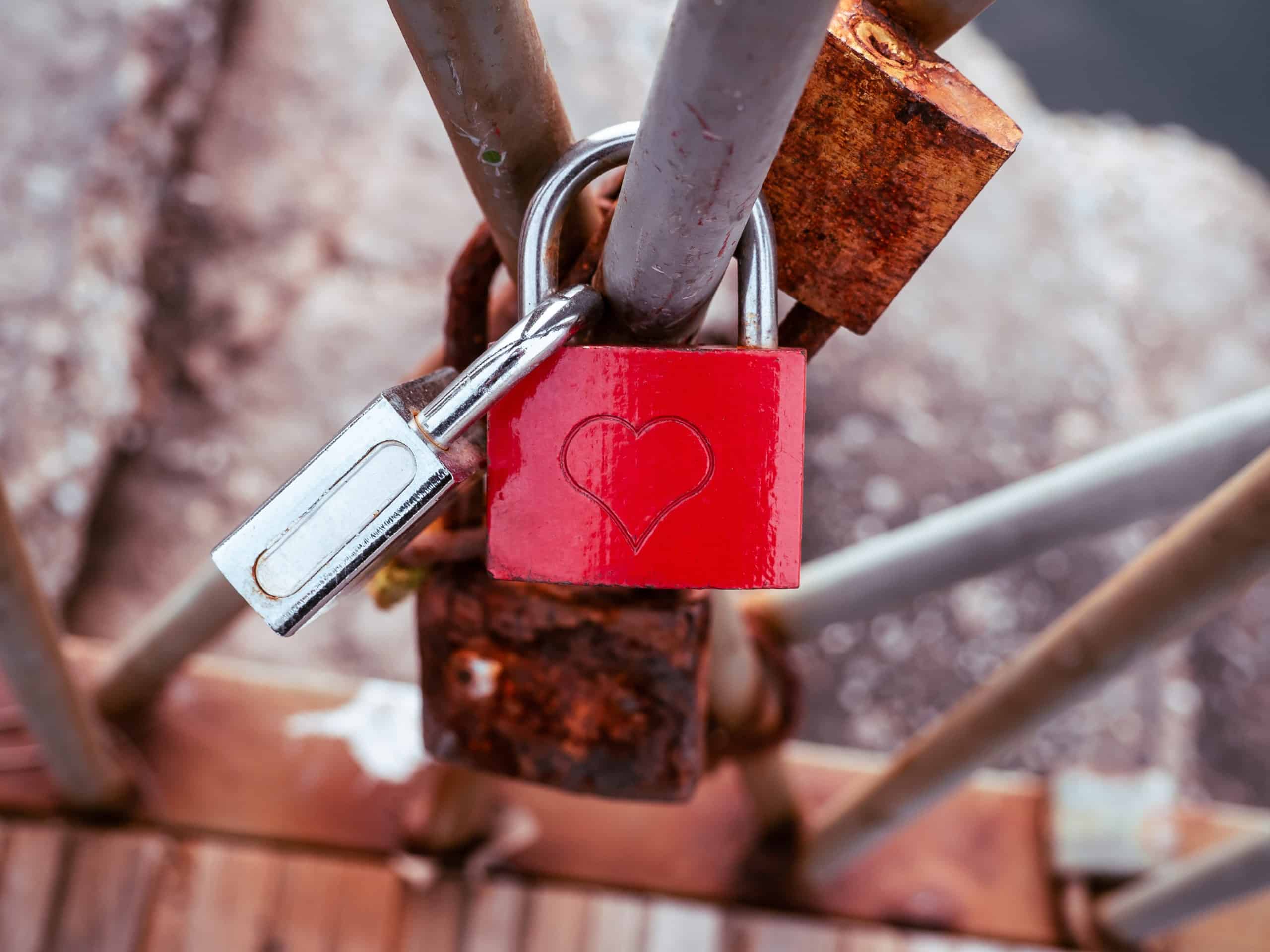 Red love lock with heart symbol, locked on a bridge rail.