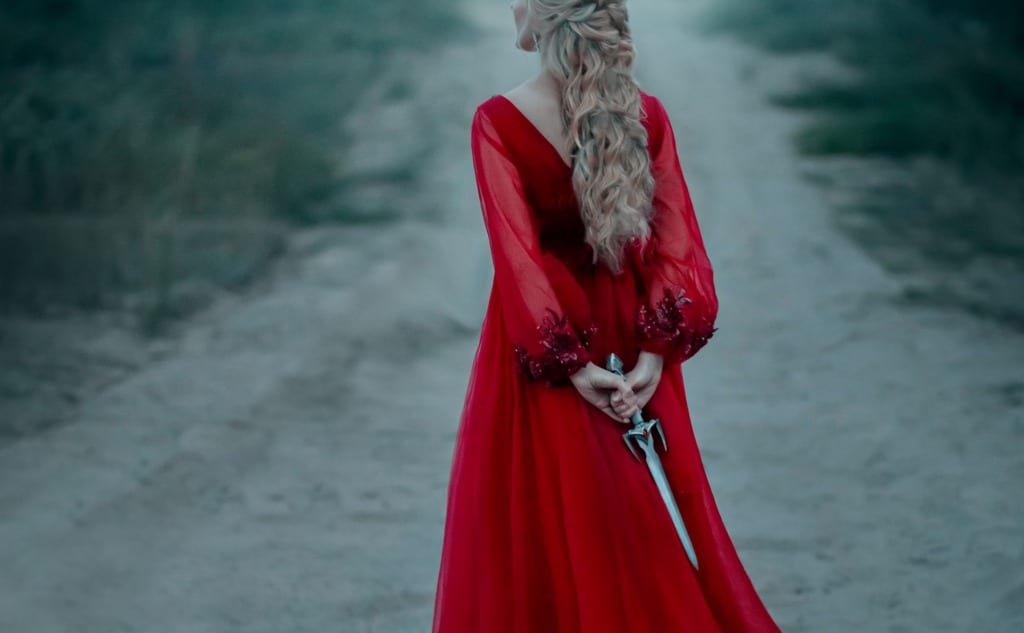 Dangerous blonde queen in red fashion lush dress Hides a dagger behind.