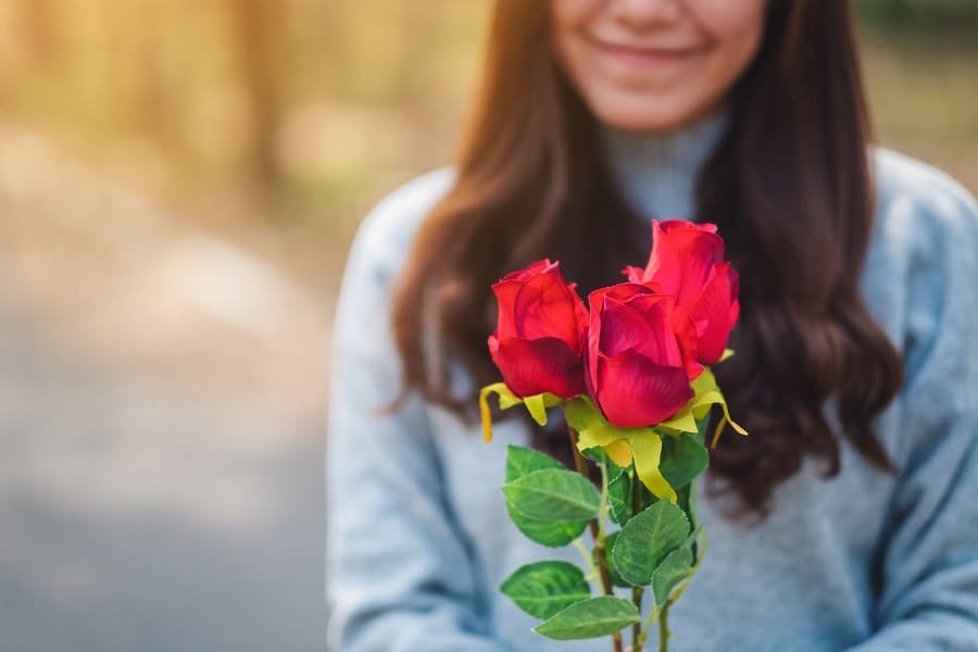 Blurry close-up of a beautiful asian woman holding red roses feeling happy on Valentine's day.