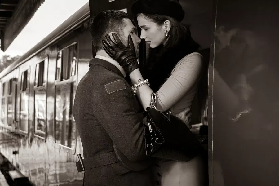 Vintage couple embracing on railway station platform as train is about to depart.