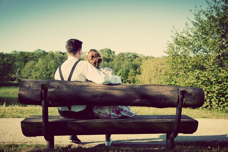 Young vintage couple in love sitting on a wooden bench in the park.