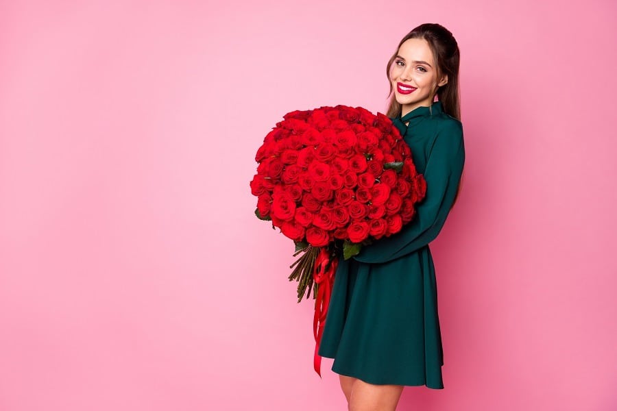 Attractive lady with red lips holds large bouquet of roses from boyfriend.
