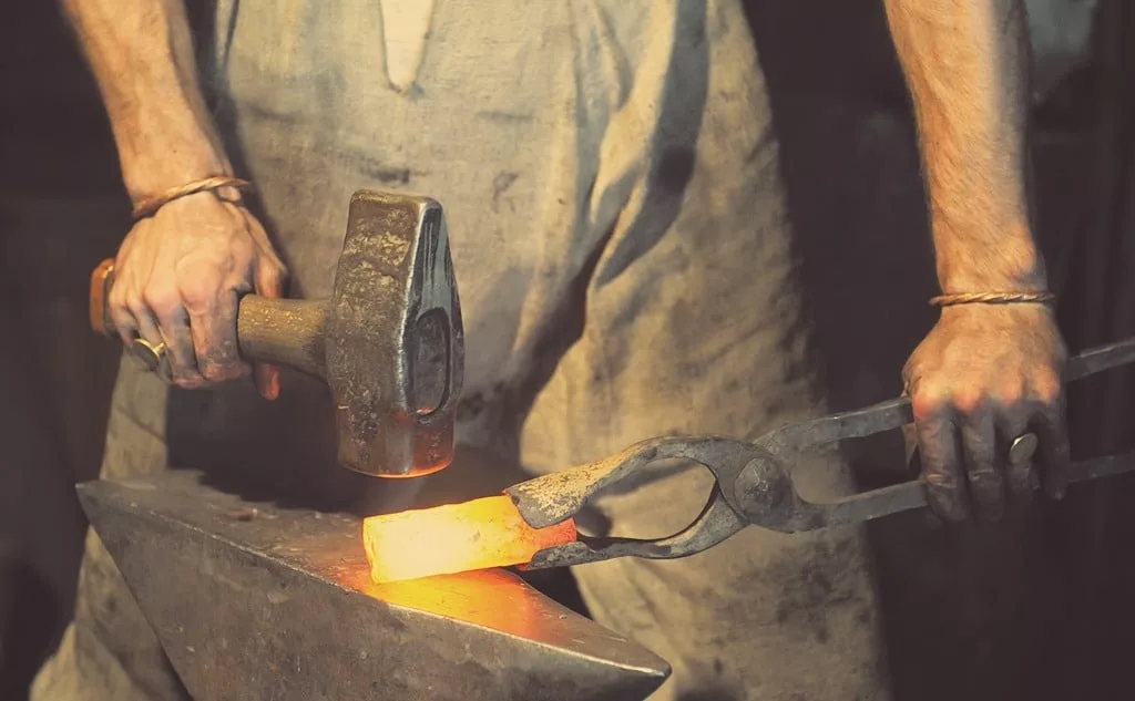 Blacksmith working metal with hammer on the anvil in the forge