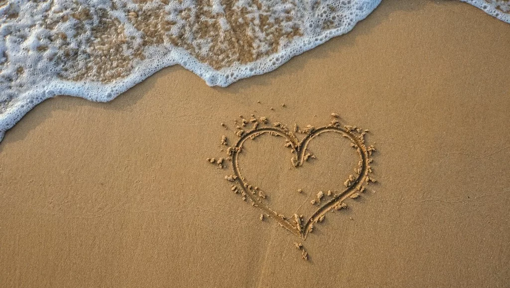 Heart drawn on the sand and frothy sea.