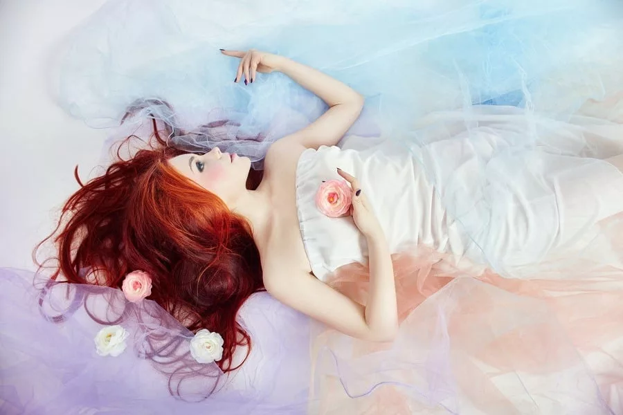 Romantic woman with red long hair wearing a sexy white dress lying on the floor heavenly background.
