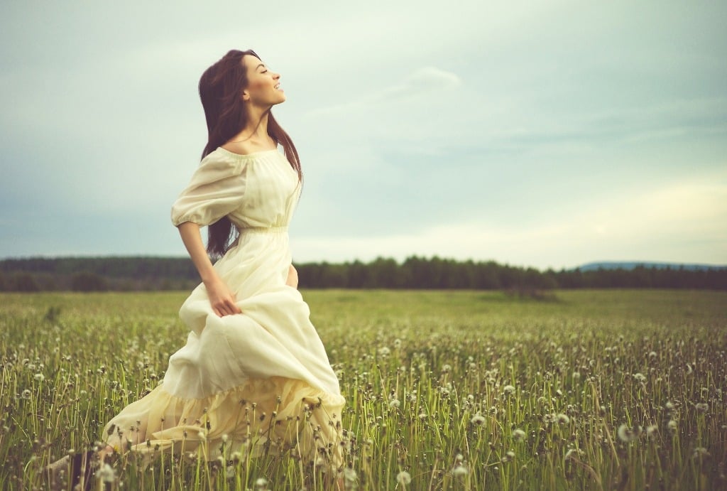 Beautiful romantic lady running on dandelions field.