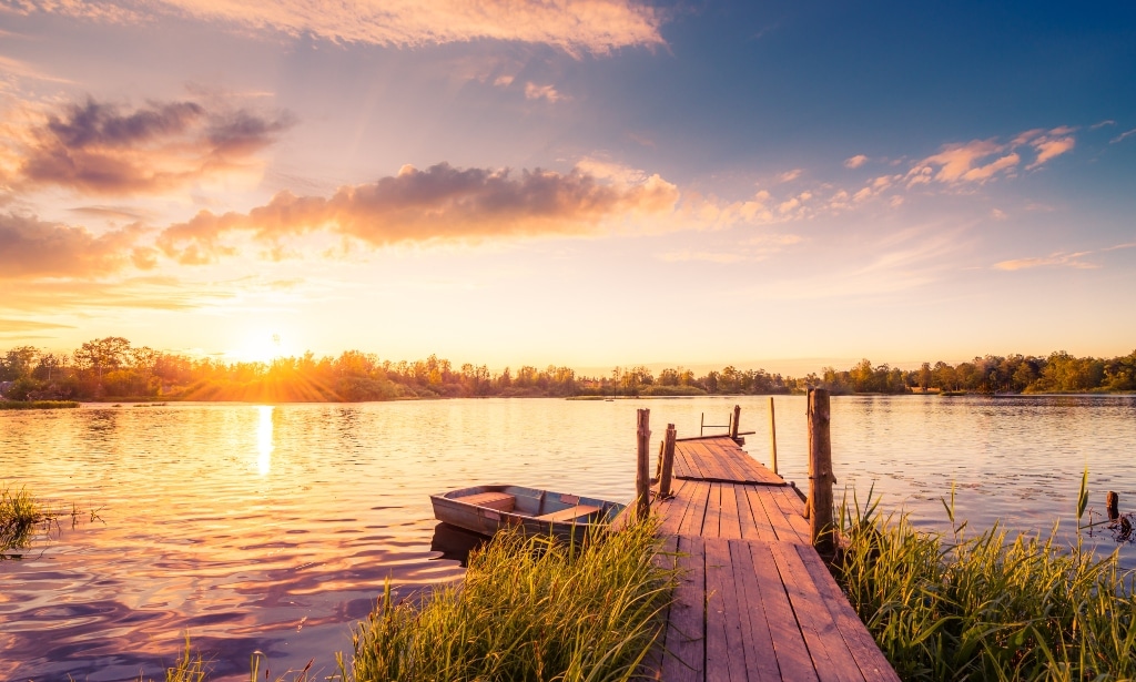 Beautiful view of a wooden dock and lake with stunning sunrise in the background.