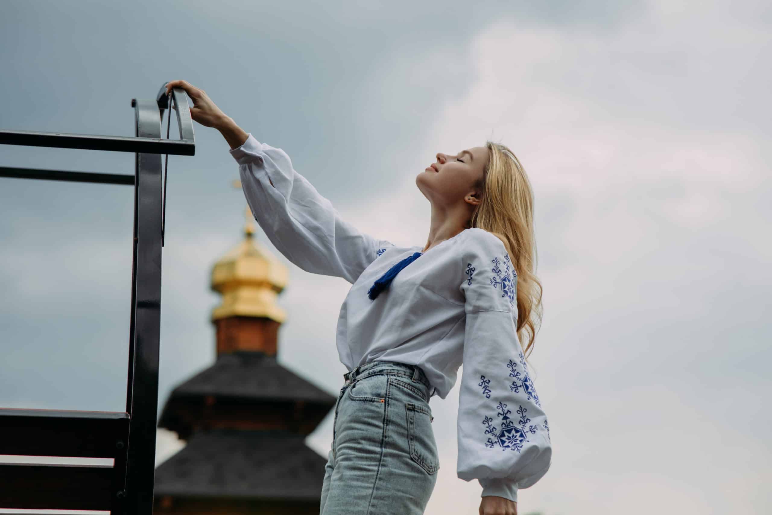 Relaxed young woman in embroidered shirt standing facing up the sky eyes closed.