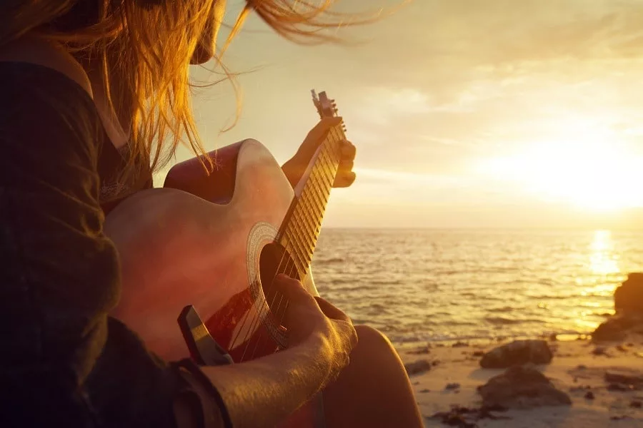 Lonesome beautiful young woman playing guitar on quiet sunset beach.