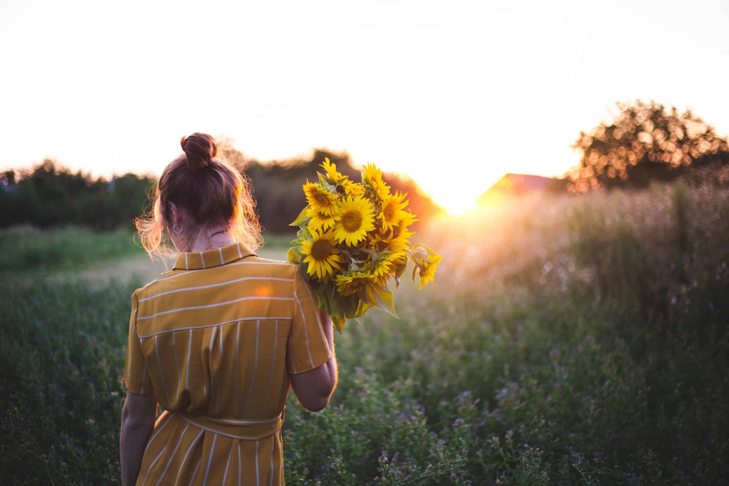 Girl outdoor carrying a bouquet of fresh sunflowers at sunrise.