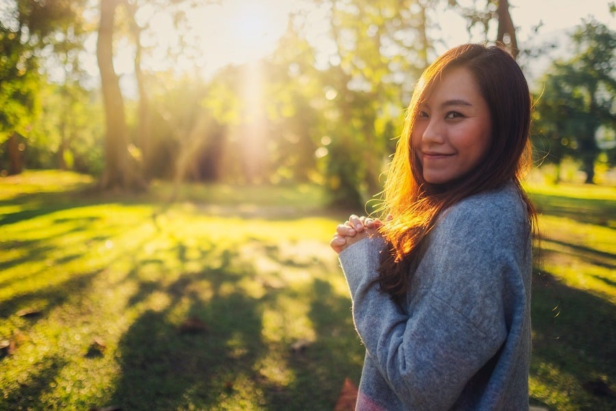 Beautiful asian woman smiling, standing at a park in bright sunlight.