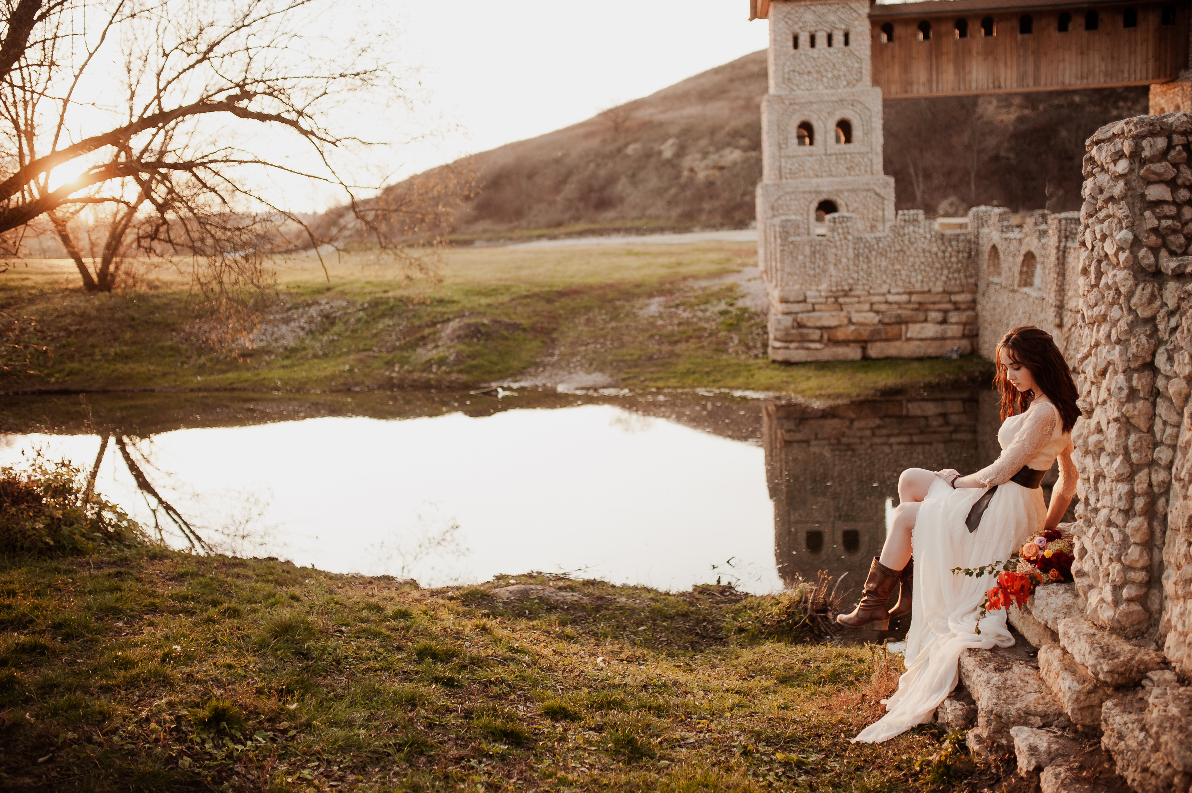 beautiful lady sits near the river against the backdrop of a stone castle