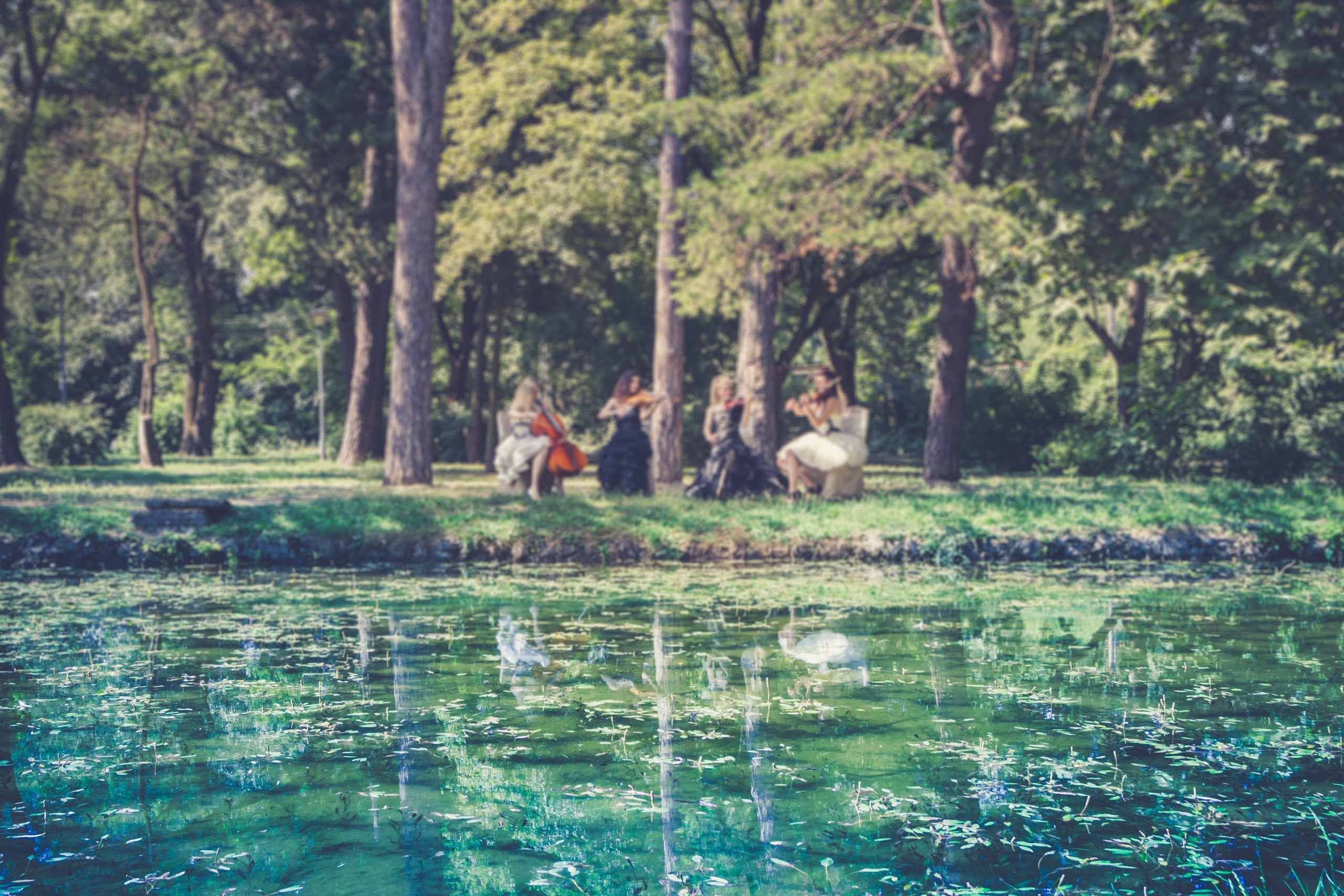 Female quartet playing music in nature by the lake.