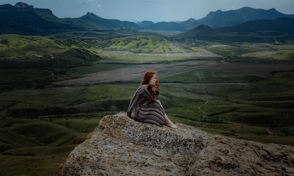 Red head woman sits alone on a cliff watching the sunset.