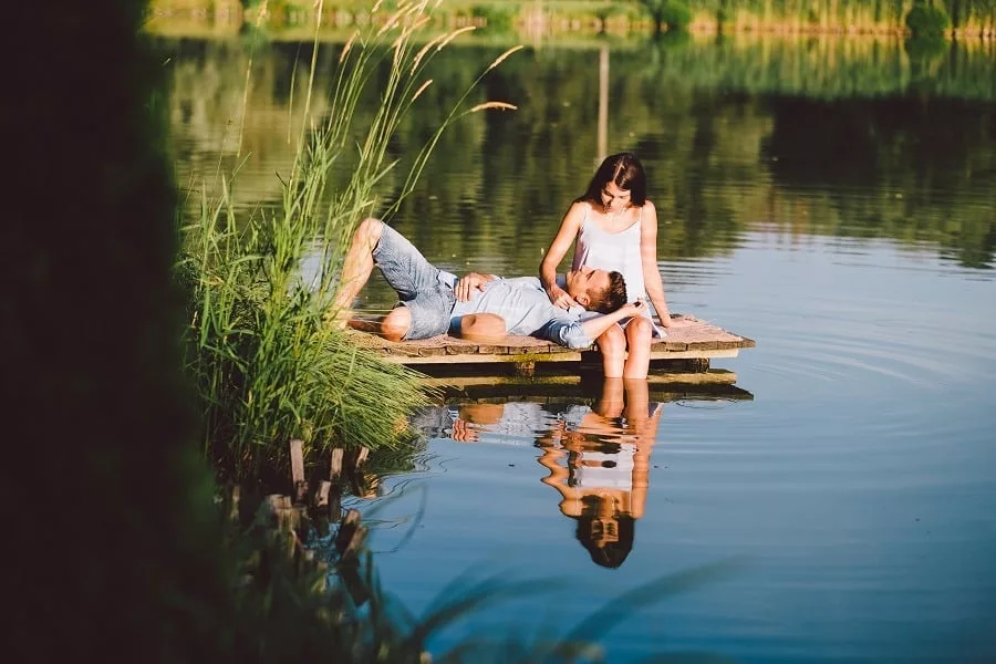 Young love couple gazing at each other man on girl's lap at the lake in summer.