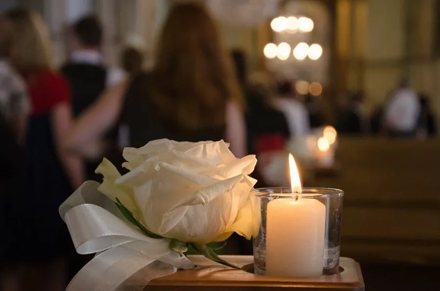 White rose and candle in a church, people in the background.