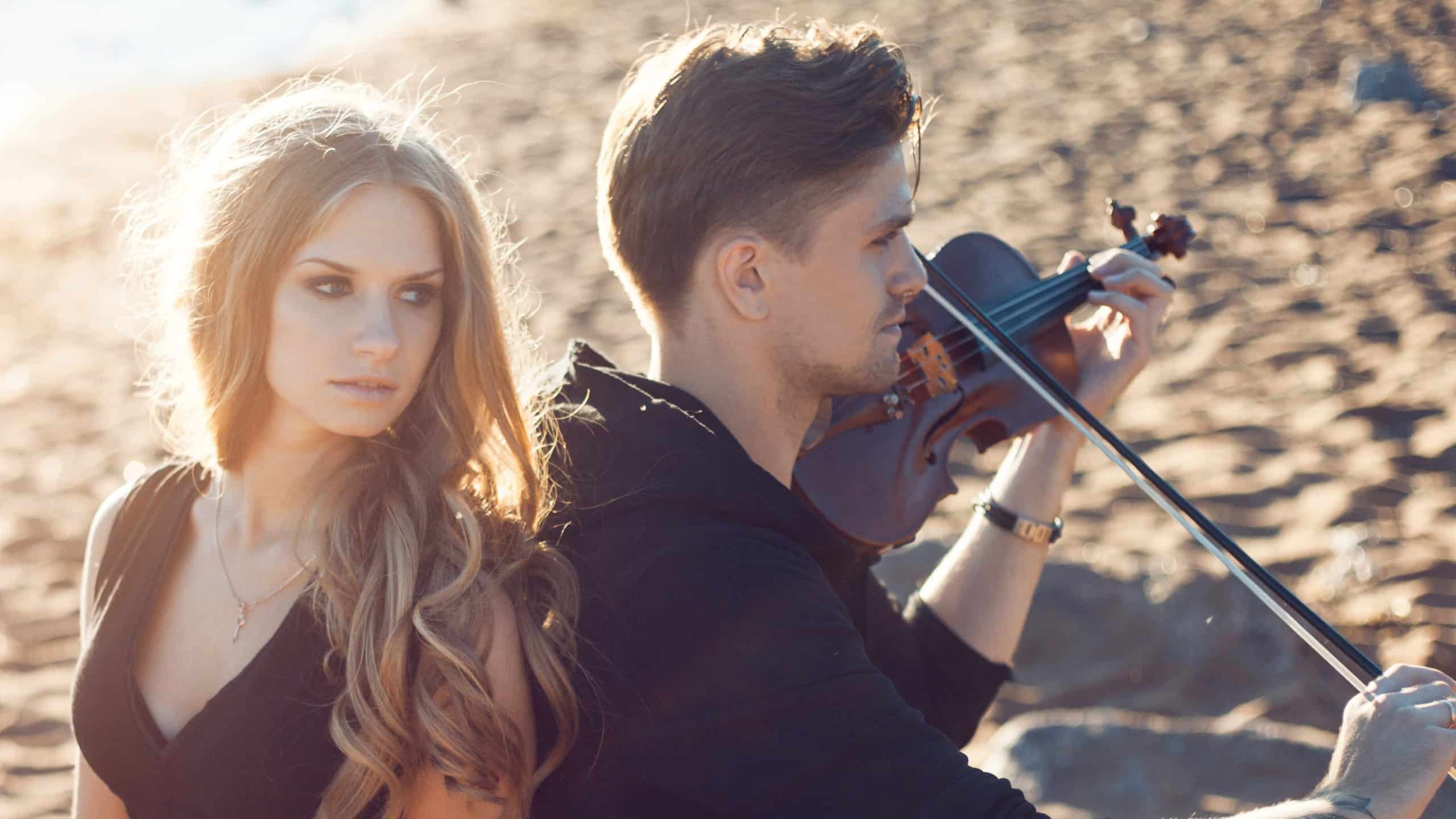 Male violinist and girl, young man plays on the background of sea.