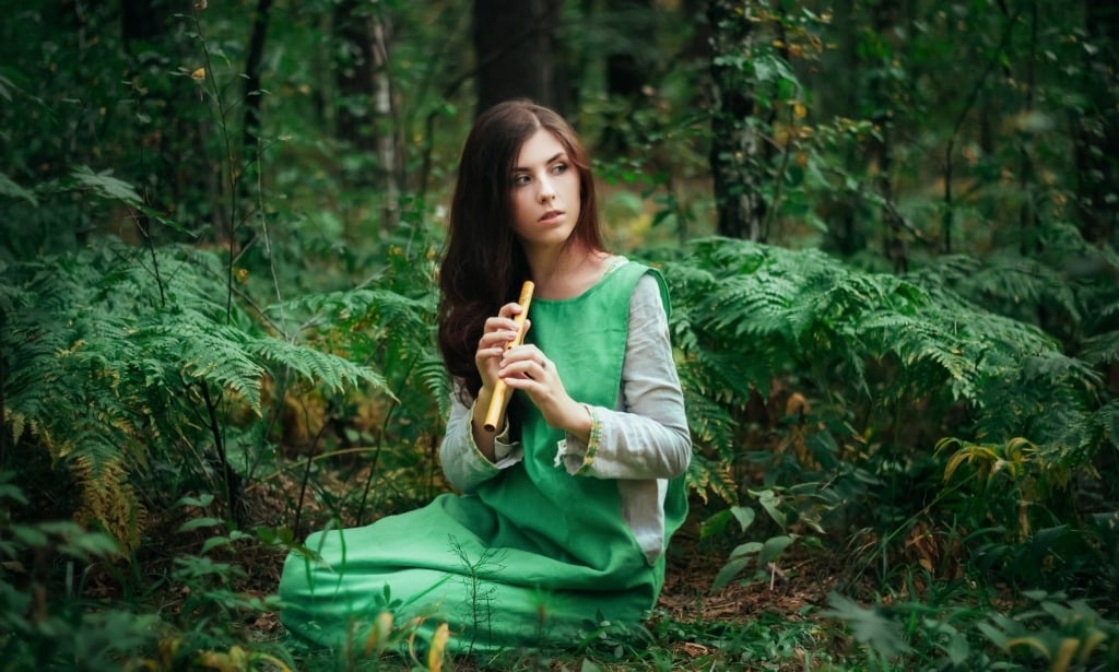 Mysterious woman seated in the forest holding a flute.