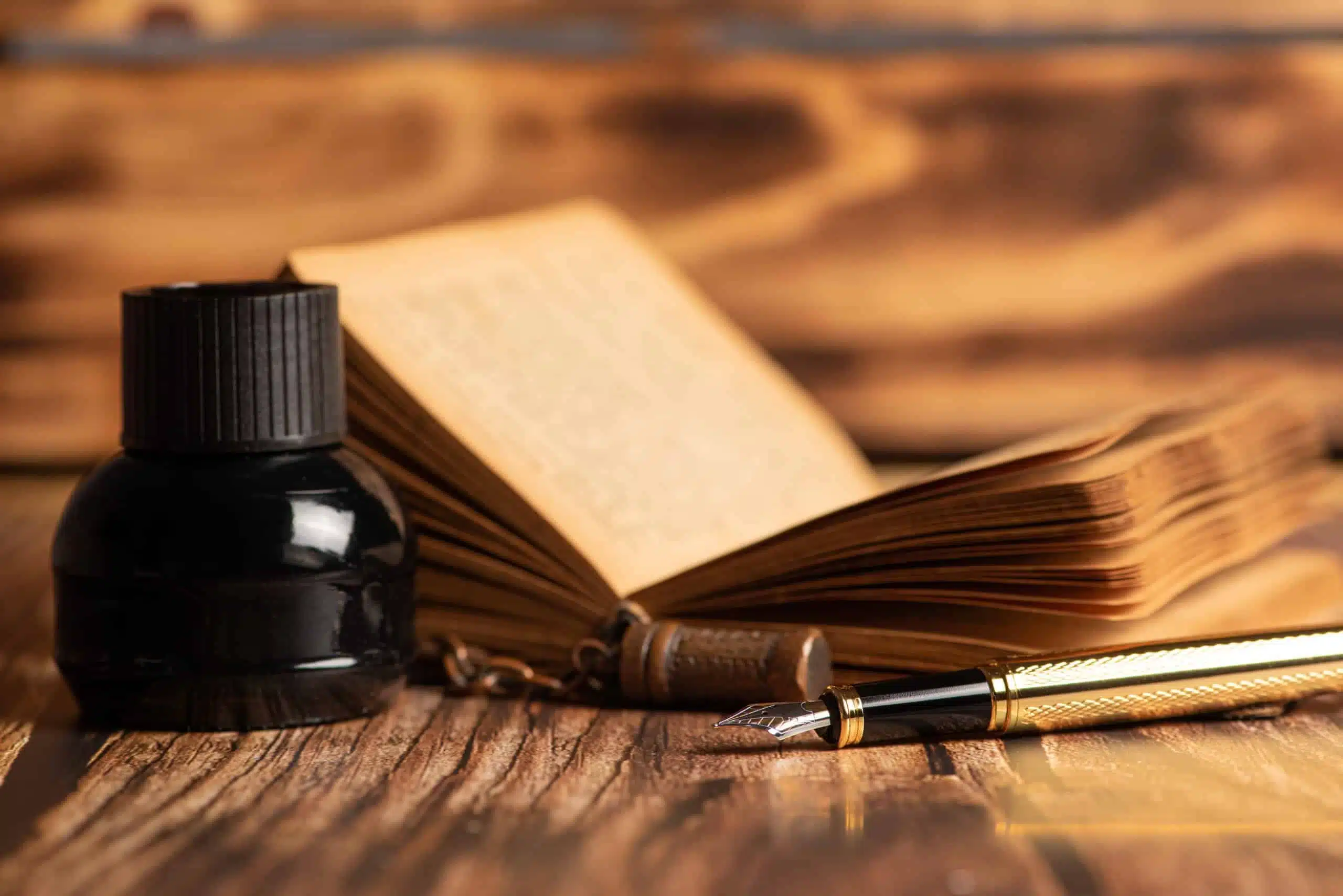 Beautiful fountain pen, book, and inkwell on wooden table.