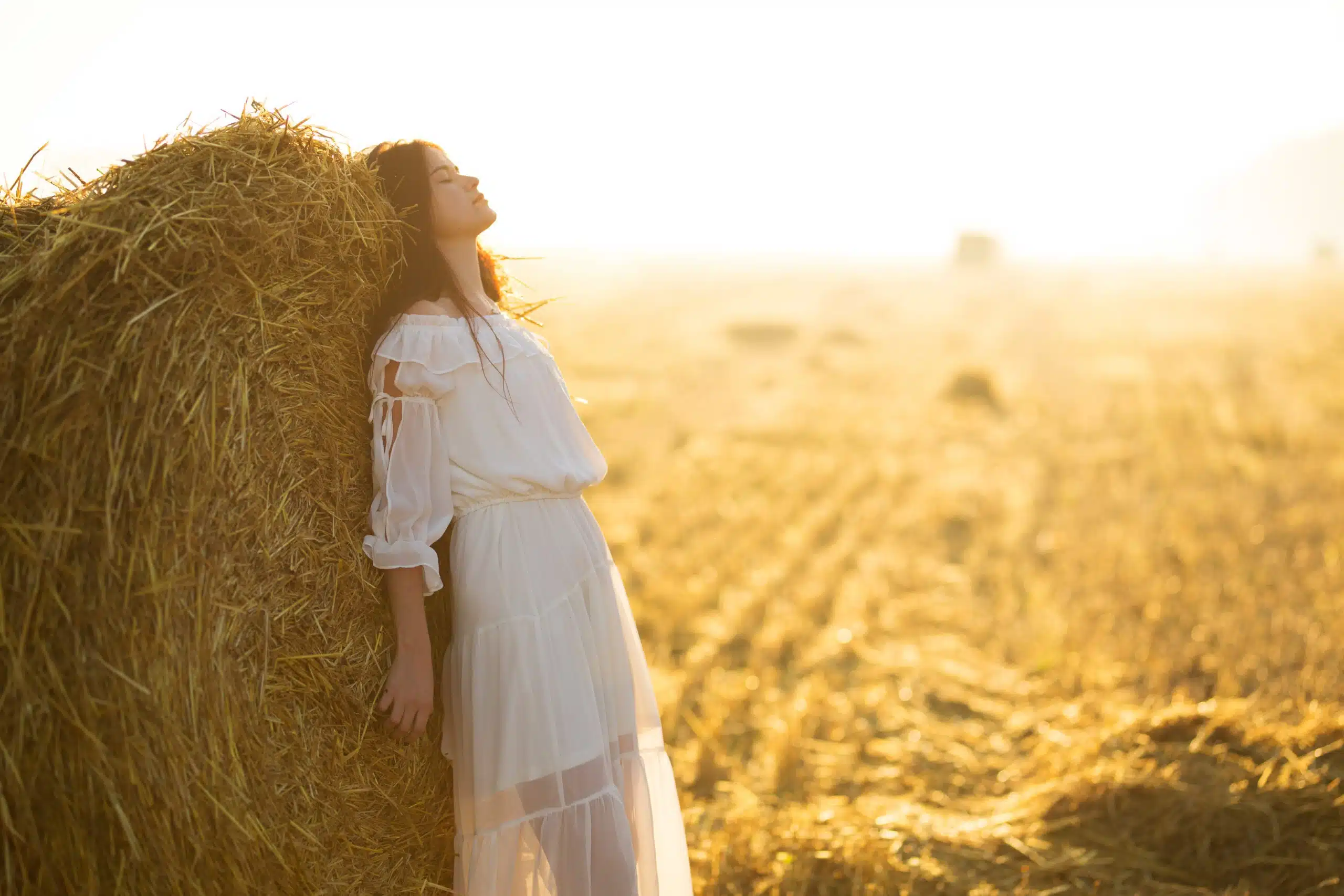 Beautiful girl in white dress running on the autumn field of wheat at sunset time.
