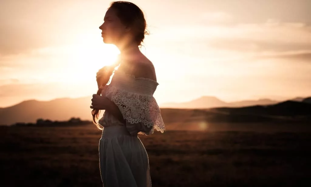 Pensive, stunning girl in white dress standing in the sunset.
