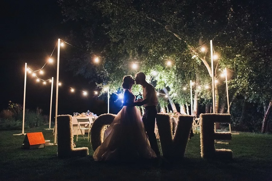 Beautiful newlyweds kiss tenderly at a wedding party with lamps.