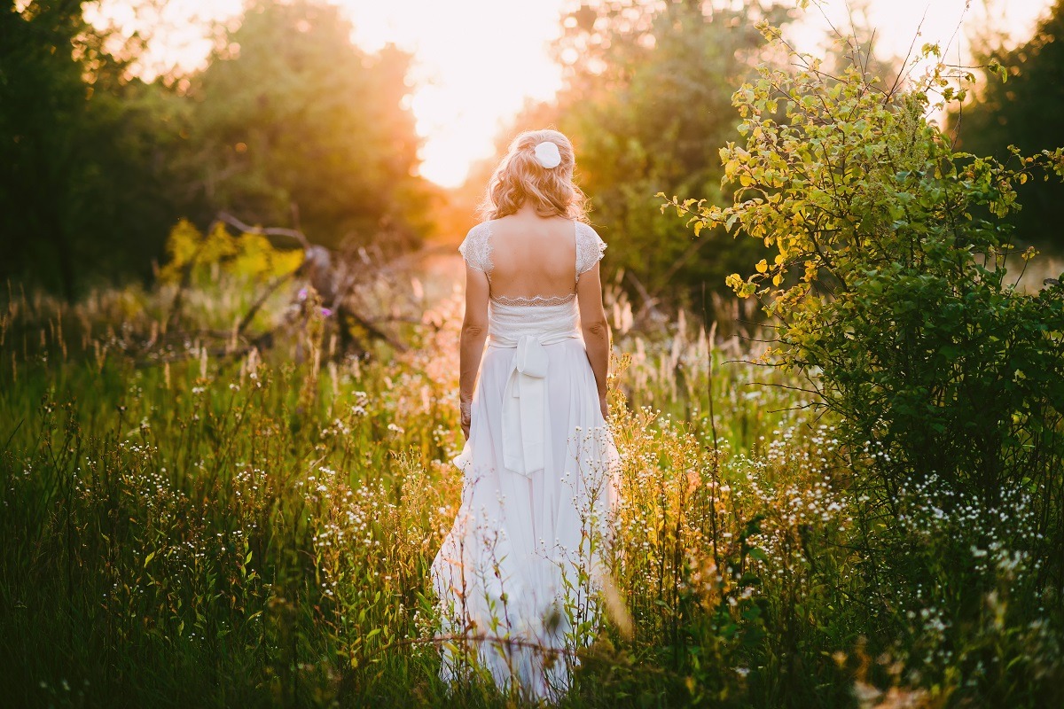 Stylish beautiful blonde bride standing in her wedding dress, walking outdoor in nature