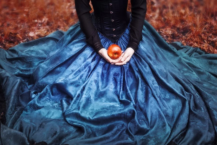 Mysterious Snow White holds a ripe apple on her lap.