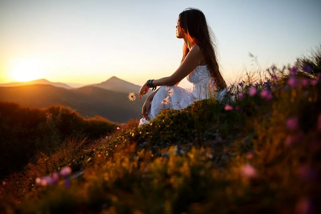 Beautiful woman in a long white dress in the mountains, hair blowing in the wind.