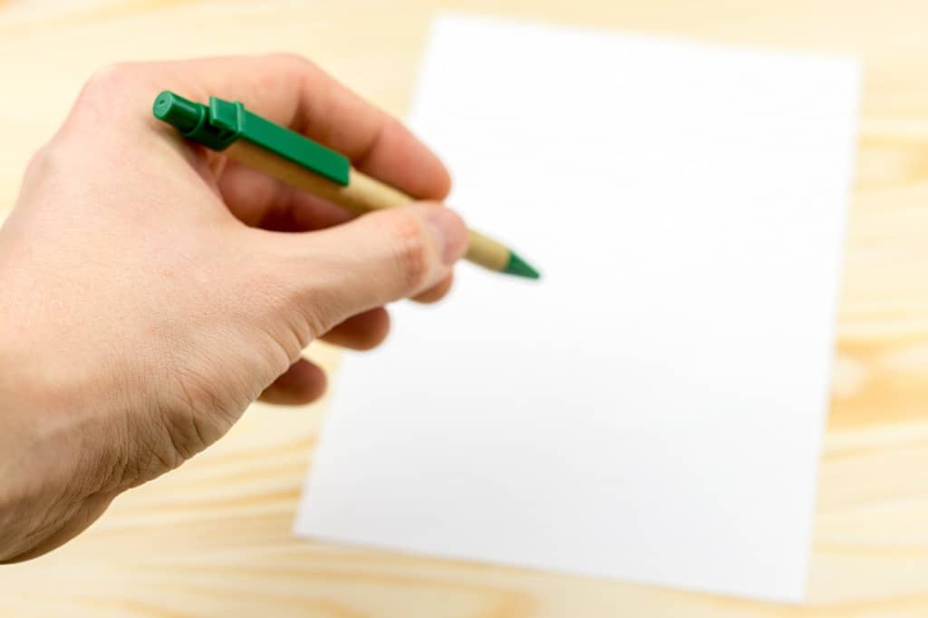 Hand holds pen on  wooden background with sheet of white paper.