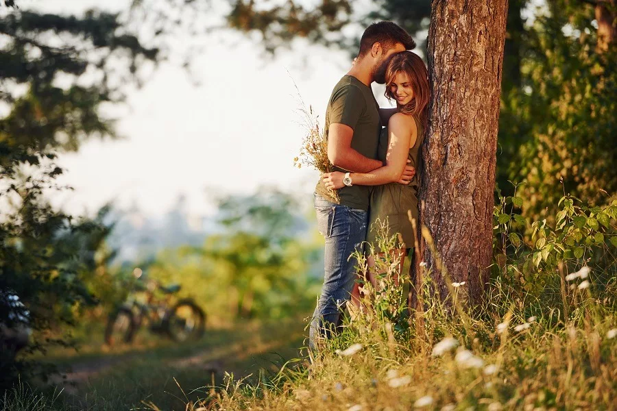 Beautiful young couple leaning on the tree having a good time in the forest at daytime.