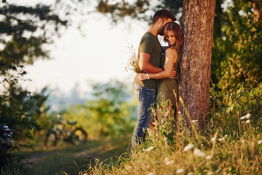 Beautiful young couple leaning on the tree having a good time in the forest at daytime.