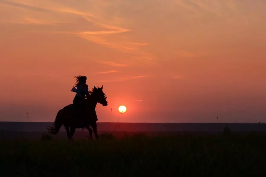 Woman horse riding with red rising sun on horizon. 