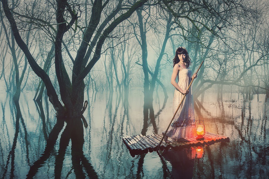 Stunning woman on a raft with a lantern floating on a pond in a misty forest.