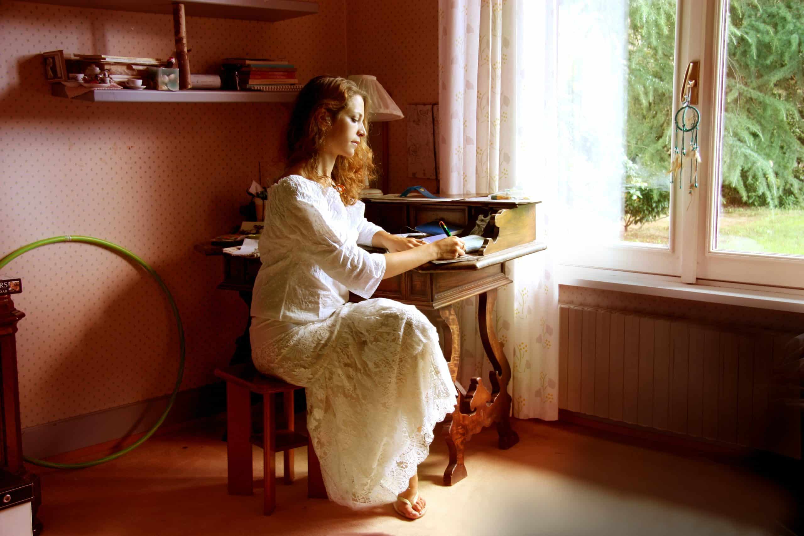 woman in white gown writes at a small table