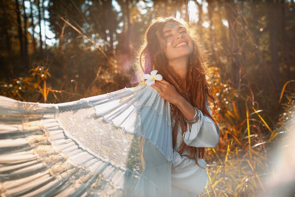 Beautiful young woman in boho style white dress outdoors at sunset