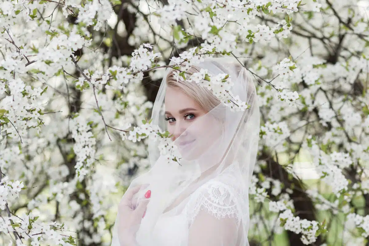 attractive lady in a lace dress and a veil standing next to a blooming tree