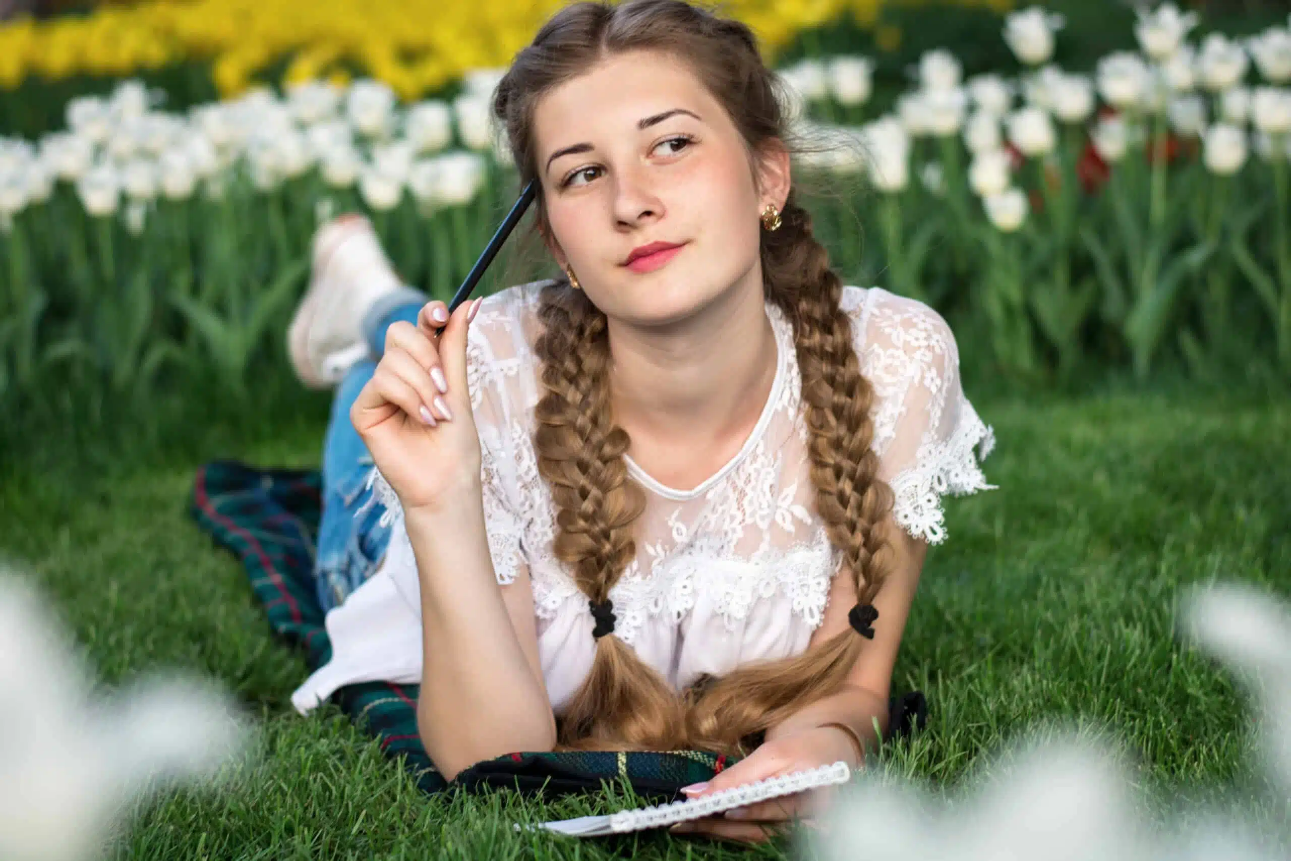 Beautiful young woman lying on the grass with pen and notepad.