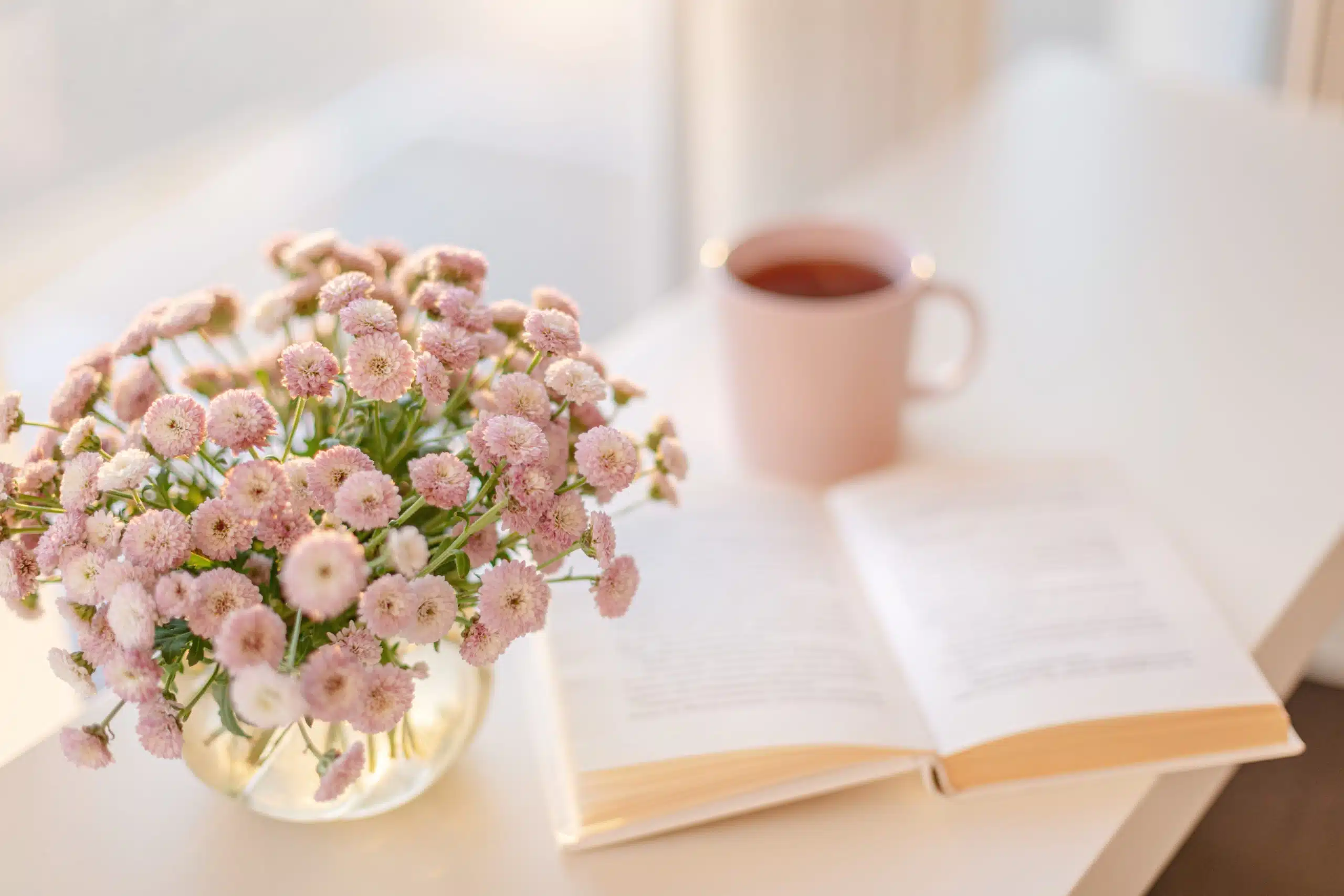 Small pink flowers bouquet in glass vase, a book and pink cup of tea