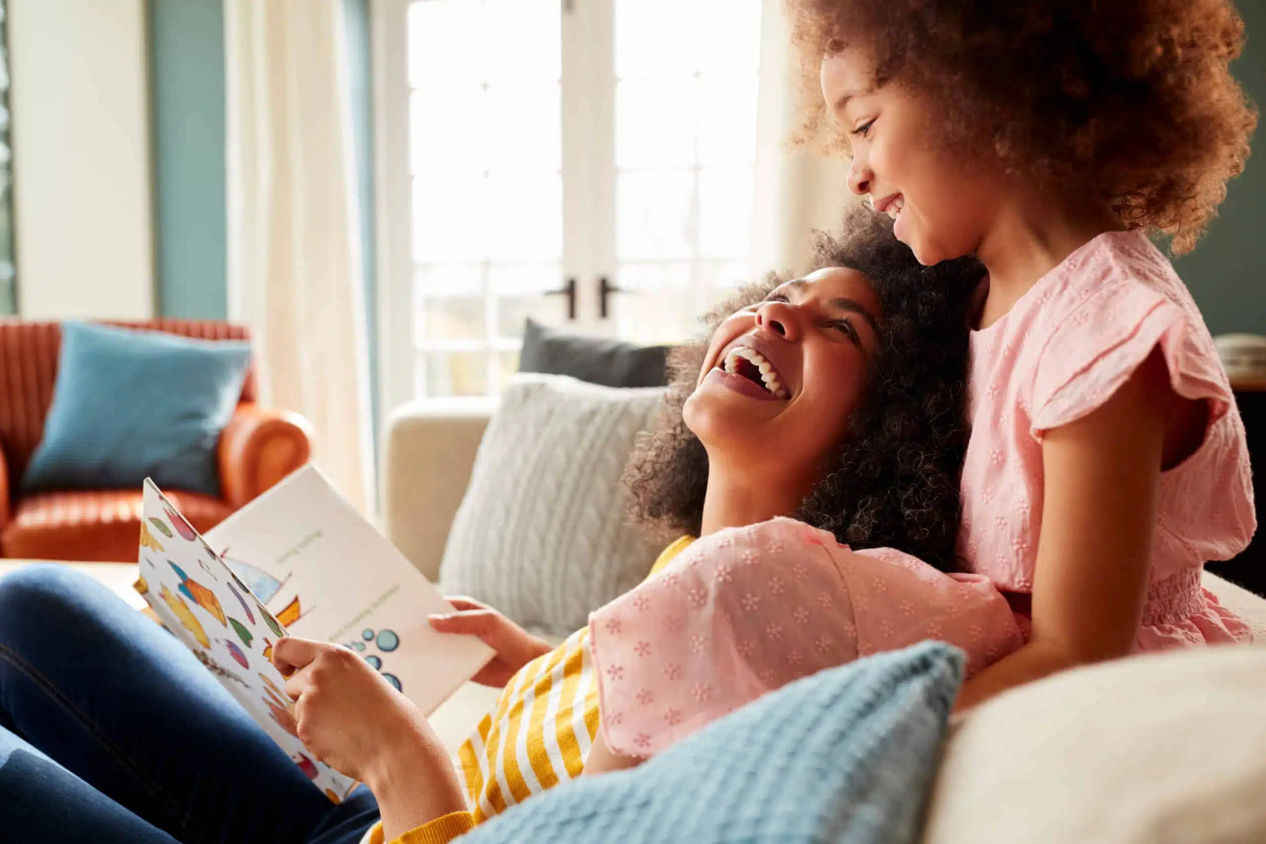 mother and daughter relaxing and reading a book together in a sofa.