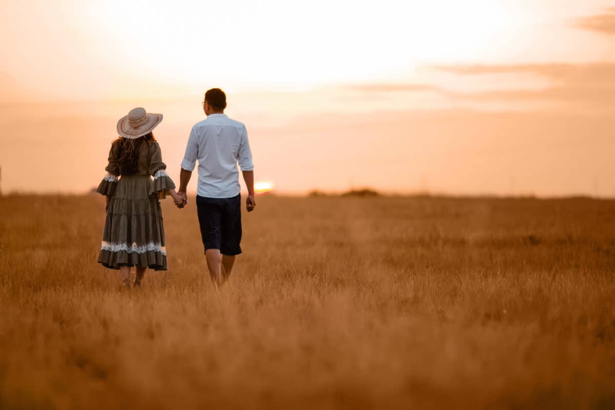 happy couple walking hand in hand in the field at sunset