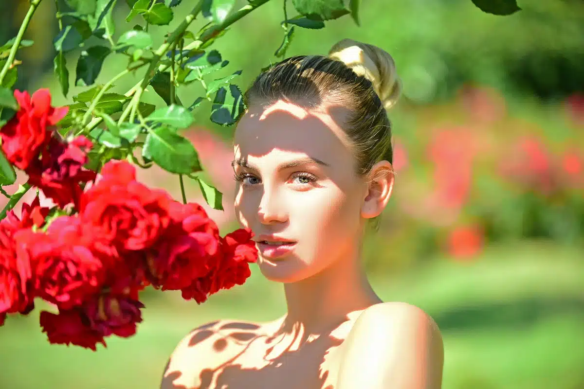 beautiful young woman standing near roses in a summer garden