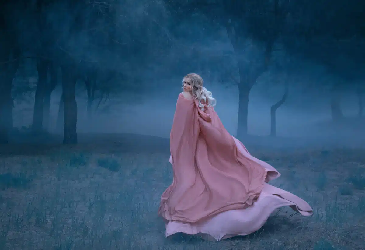 Gorgeous young queen with blond hair runs in a dark and dense scary forest full of white mist, dressed in a long, flying and flowing peach dress, a photograph of a beautiful woman in the moonlight