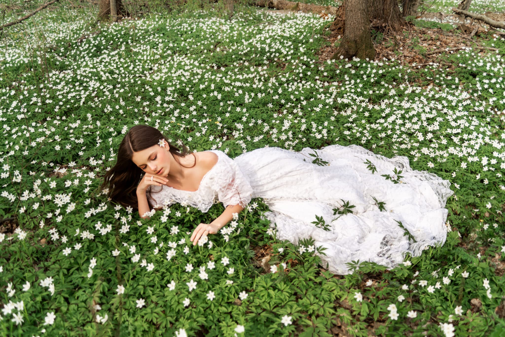 girl in a white lace dress lies in a clearing with primroses. 