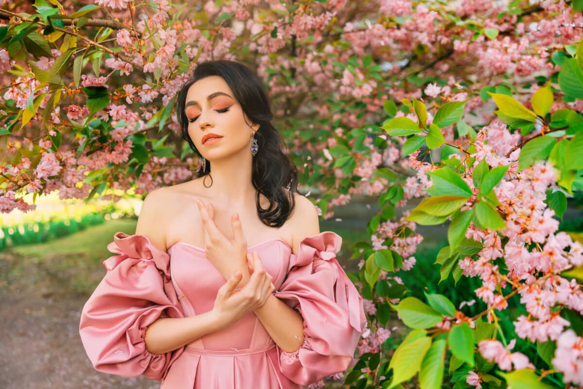 Portrait Fantasy girl princess in blooming spring garden flowers sakura tree green grass. Happy woman queen beauty face Lady in romantic pink sexy dress bare open shoulders vintage old style art photo