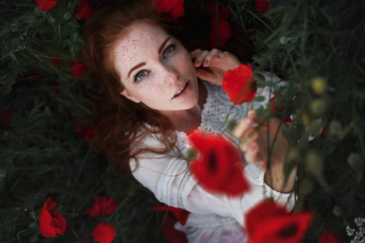 a beautiful red haired woman looking up among red poppies in the field