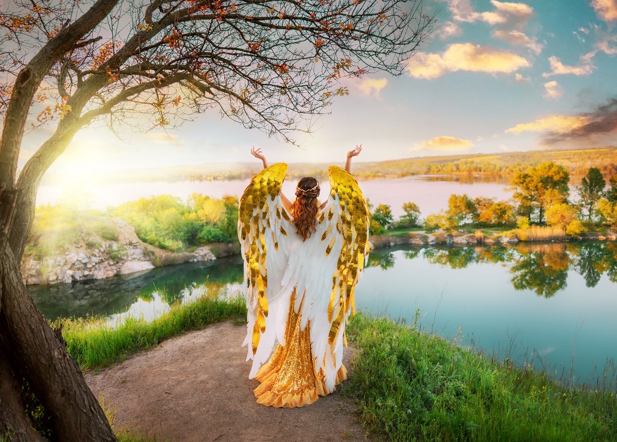 fantasy angel goddess raises her hands to the bright golden sky from atop a mountain